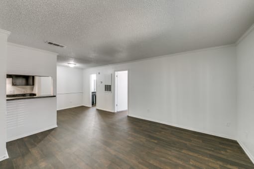 an empty living room and kitchen with wood flooring and white walls