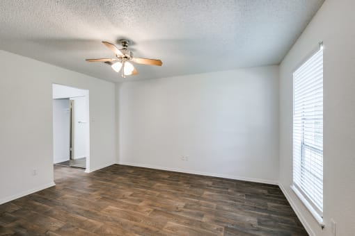 an empty living room with a ceiling fan and a window