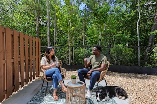 Two people sitting on chairs in a backyard with a dog lying on the ground.