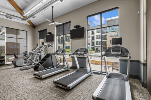 a gym with cardio equipment and windows with a view of the city