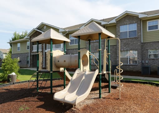 a playground with a slide and swings in front of a house