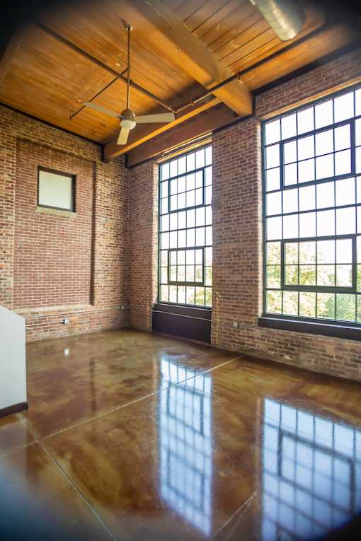 A room with a ceiling fan and large windows.