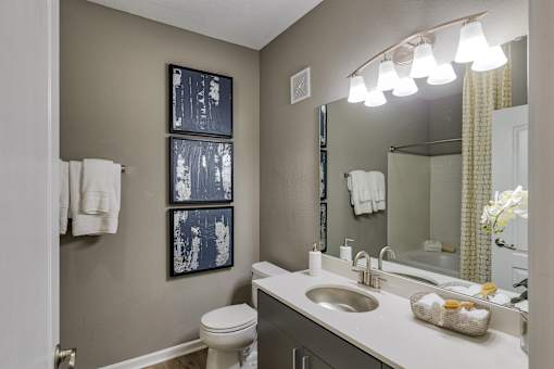 A bathroom with a toilet, sink, mirror, and two towels hanging on the wall.