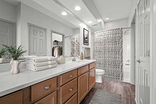 A bathroom with a white countertop and a shower with a black and white patterned shower curtain.