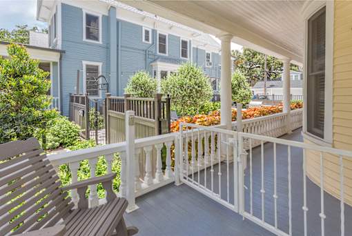 A wooden bench sits on a porch with a white railing.