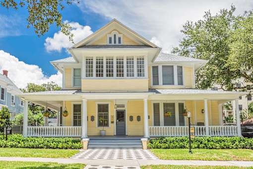 A yellow house with a white porch and a grey door.