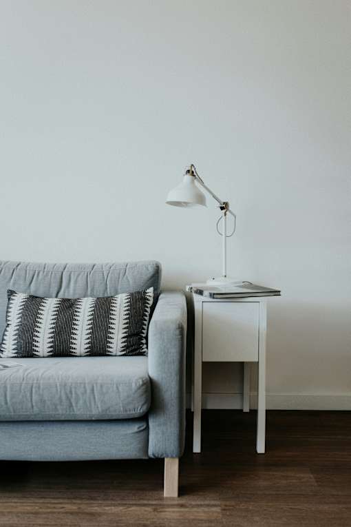 A grey couch with a white table and lamp beside it.