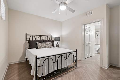 A bedroom with a bed, pillows, a ceiling fan, and a doorway leading to a bathroom.