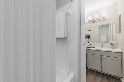 A white bathroom with a sink, mirror, and a towel hanging on the wall.