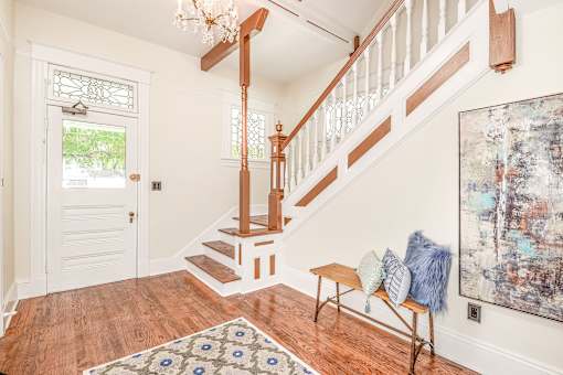 A staircase with a wooden banister and a chandelier hangs over a hardwood floor.