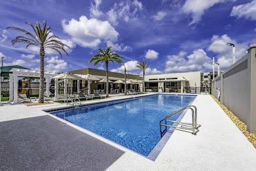 A large outdoor swimming pool surrounded by palm trees and a building.