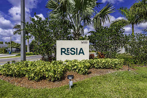 A sign that says "RESIA" in front of a green bush.