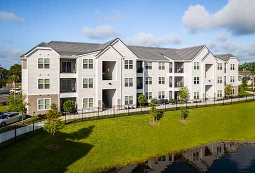 A large white building with a black fence and a pond in front.