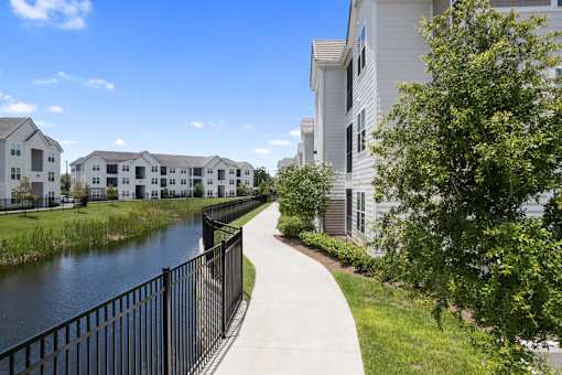 A walkway runs alongside a body of water with apartment buildings on either side.