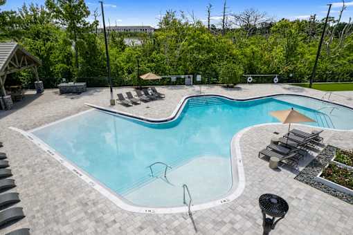 A large outdoor swimming pool surrounded by trees and lounge chairs.