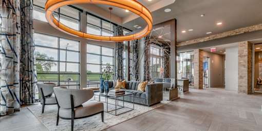 A modern living room with a large circular light fixture and a view of the outdoors through the windows.