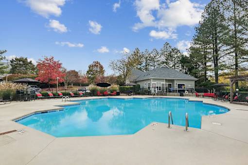 A large swimming pool with a blue tinted water surrounded by trees and a building in the background.