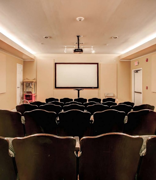 A row of seats in a theater with a large screen above.