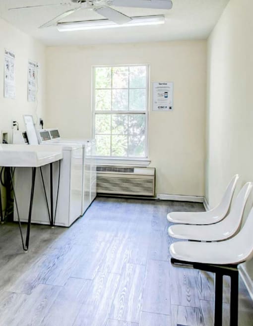 A room with a white desk, chairs, and a window.