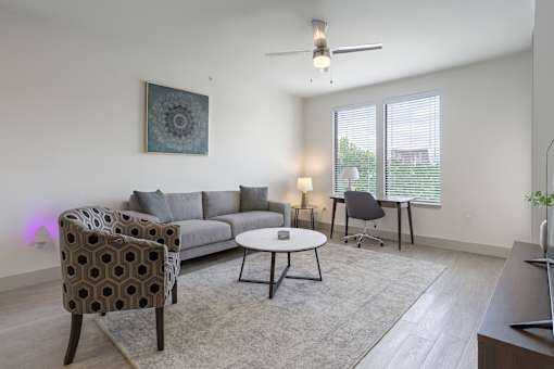 A living room with a grey sofa, a patterned chair, a small table, and a ceiling fan.