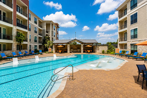 A swimming pool surrounded by a patio with chairs and umbrellas.
