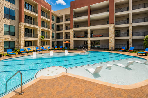 A large swimming pool in front of a multi-story apartment building.