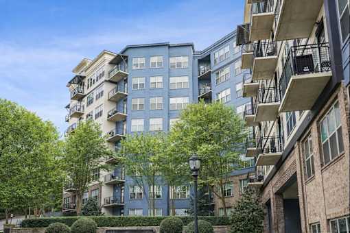 A tall apartment building with balconies and trees in front.