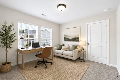A room with a desk, chair, and a couch with a picture on the wall.
