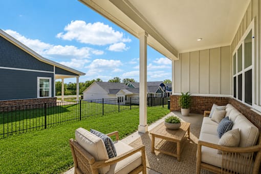 A patio with a sofa and chairs overlooking a green lawn and a blue house.