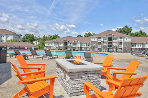 A fire pit sits in front of orange chairs in a pool area.