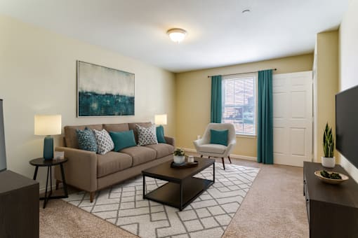 A living room with a beige couch, a painting on the wall, and a patterned rug.