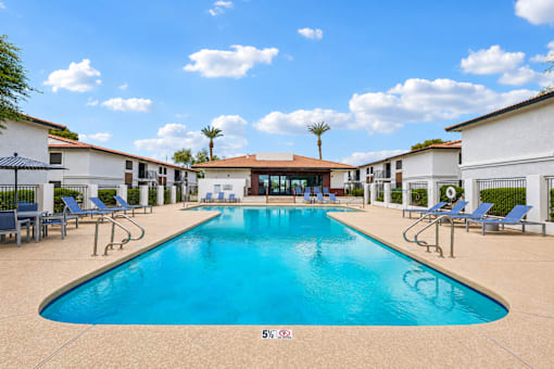 A large swimming pool surrounded by lounge chairs and buildings.