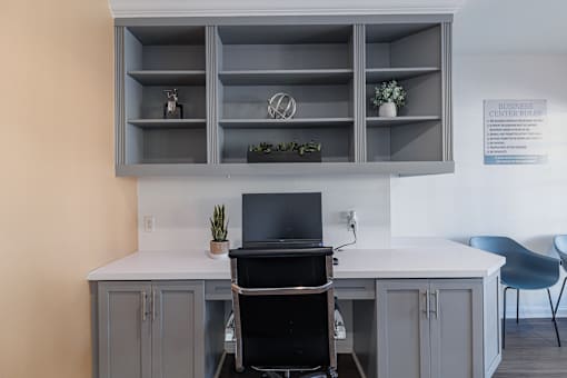 A white desk with a black chair and a black laptop on it.