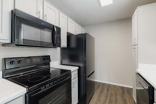 A black microwave is mounted above a black stove in a kitchen with white cabinets.