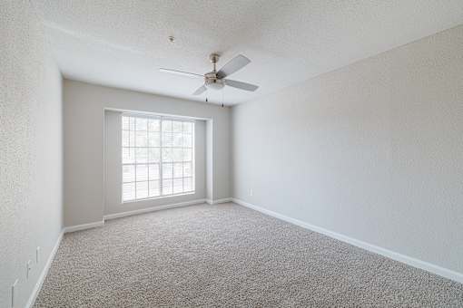 A room with a carpet floor, a ceiling fan, and a window.