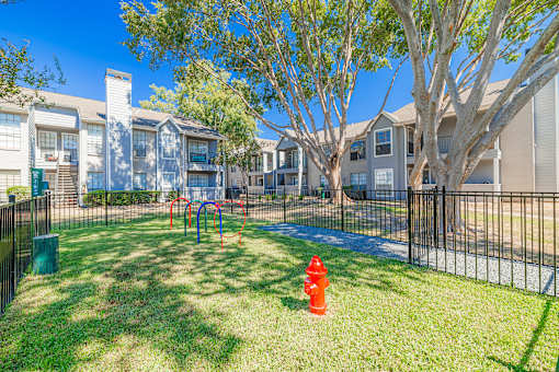 A playground with a red slide and a red fire hydrant in a grassy area in front of apartment buildings.