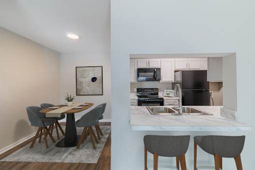 A kitchen with a table and chairs in the foreground and a microwave, oven, and sink in the background.
