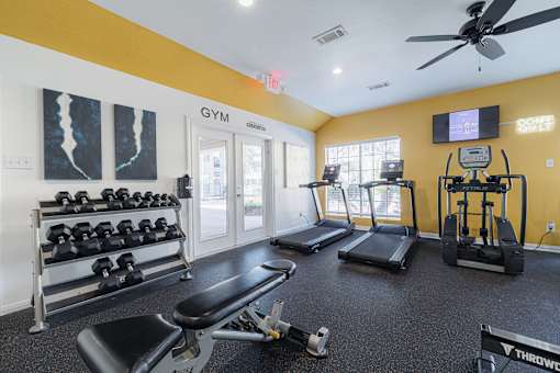 A gym with a variety of equipment including dumbbells, treadmills, and a bench press.
