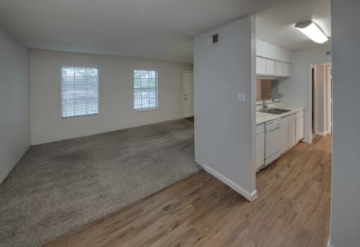 an empty living room and kitchen with wood flooring and white cabinets