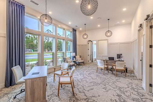 A room with a desk, chairs, and a large window overlooking a green area.