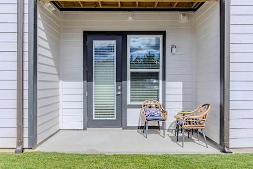 A white house with a black door and two chairs on the porch.
