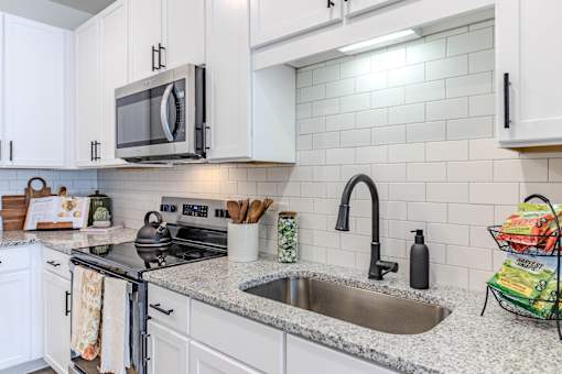 A kitchen with a stove, microwave, and white cabinets.