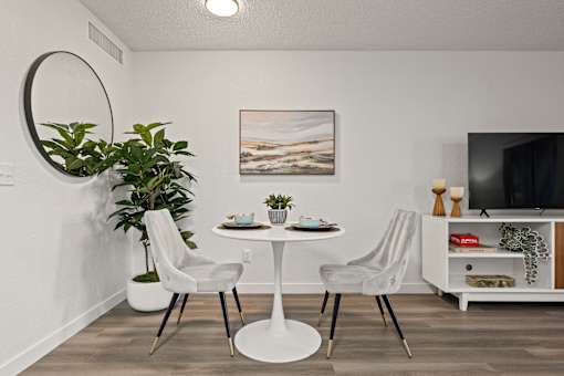 A white dining table with two chairs and a potted plant in a modern room.