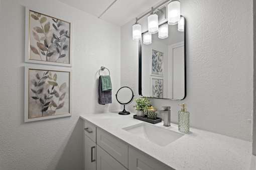 A bathroom with a white sink and a mirror with lights above it.