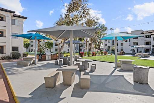 A sunny day at a park with concrete benches and umbrellas.