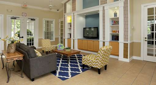 A living room with a grey couch, yellow and white chairs, a wooden coffee table, and a television.