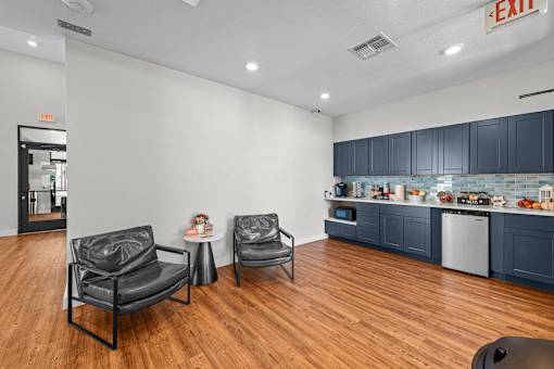 a living room with two chairs and a kitchen with blue cabinets