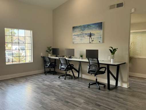 A room with a long table and chairs, a plant, and a painting of a person on a surfboard.