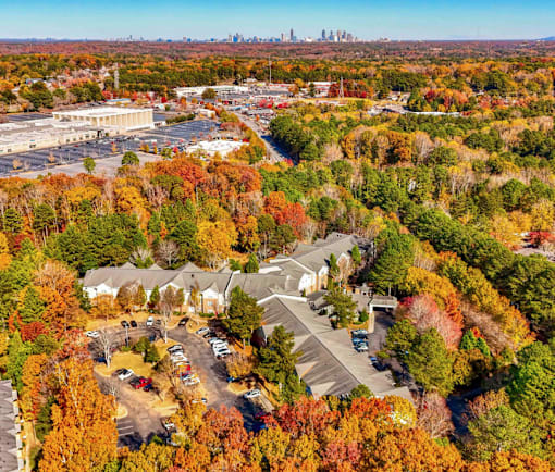 An aerial view of a suburban area with a parking lot and houses surrounded by trees in autumn colors.