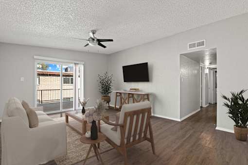 A living room with a white couch, a wooden chair, a small table, a television, and a potted plant.